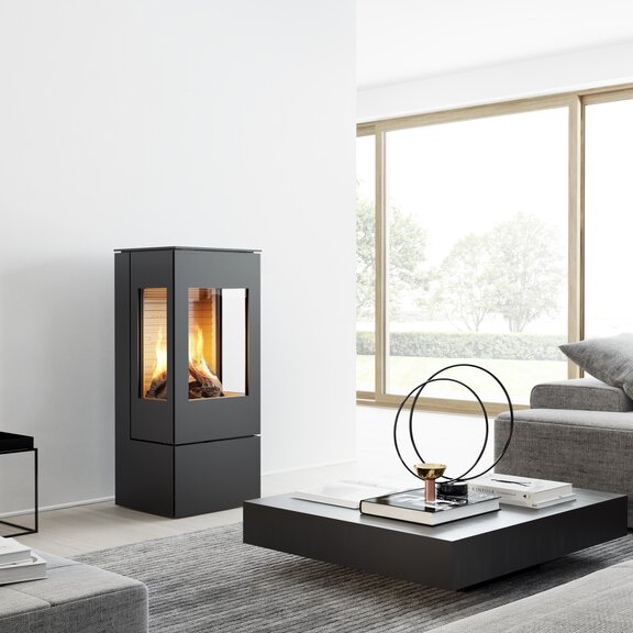 Gas stove NEXO 100 in black with steel door and two side windows in a modern, bright living room