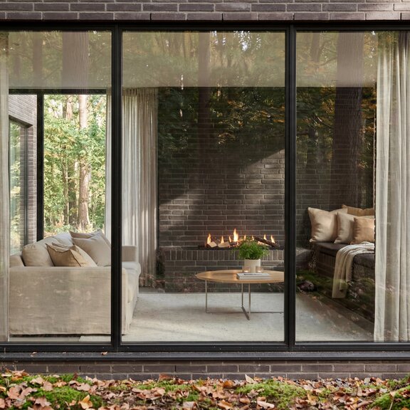 Logicwood Linear Bioethanol fireplace built into a dark stone wall, view through the window into the living room