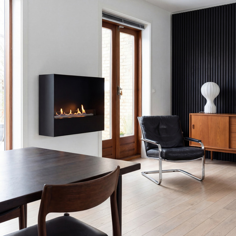 Bioethanol fireplace Milan with a black front panel, wall-mounted in a room featuring a black leather armchair and a wooden table